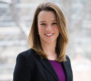 Kate, a white woman who has shoulder-length blonde hair. She is wearing a purple top and black blazer.